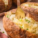 A fork digging into a hot baked potato, showing the fluffy texture with melted butter and green onion.
