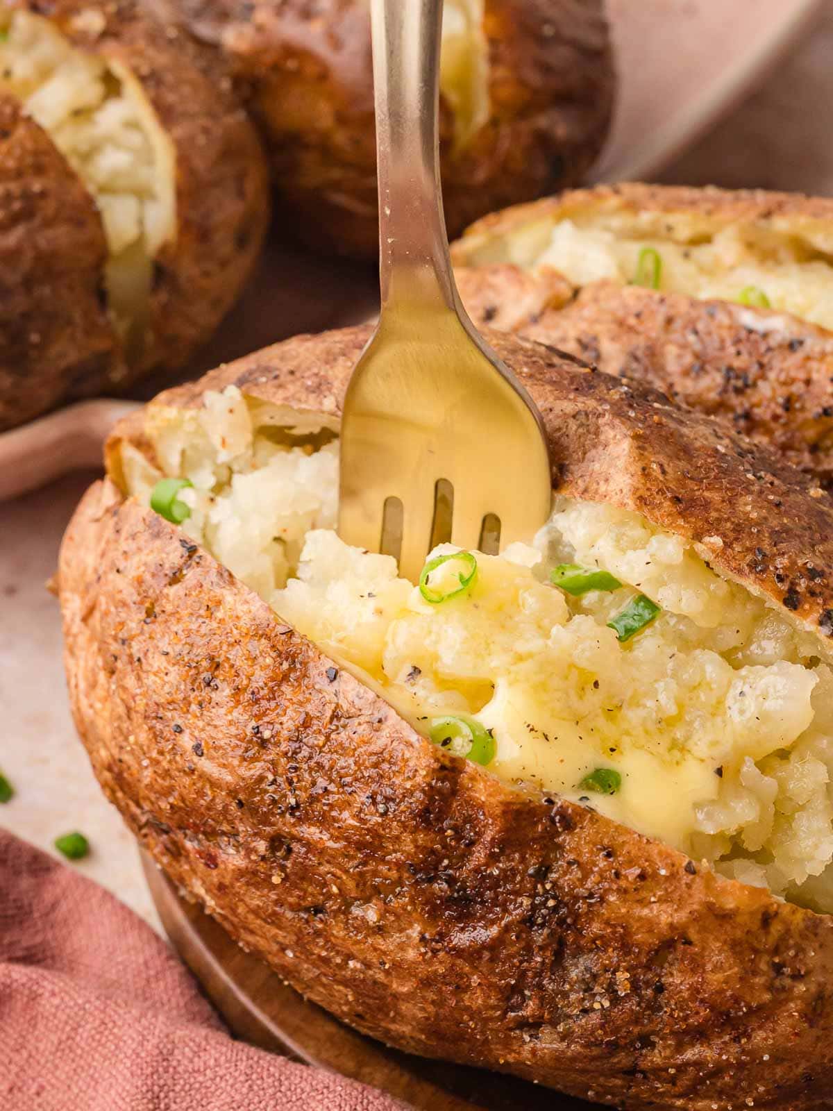 A fork digging into a hot baked potato, showing the fluffy texture with melted butter and green onion.