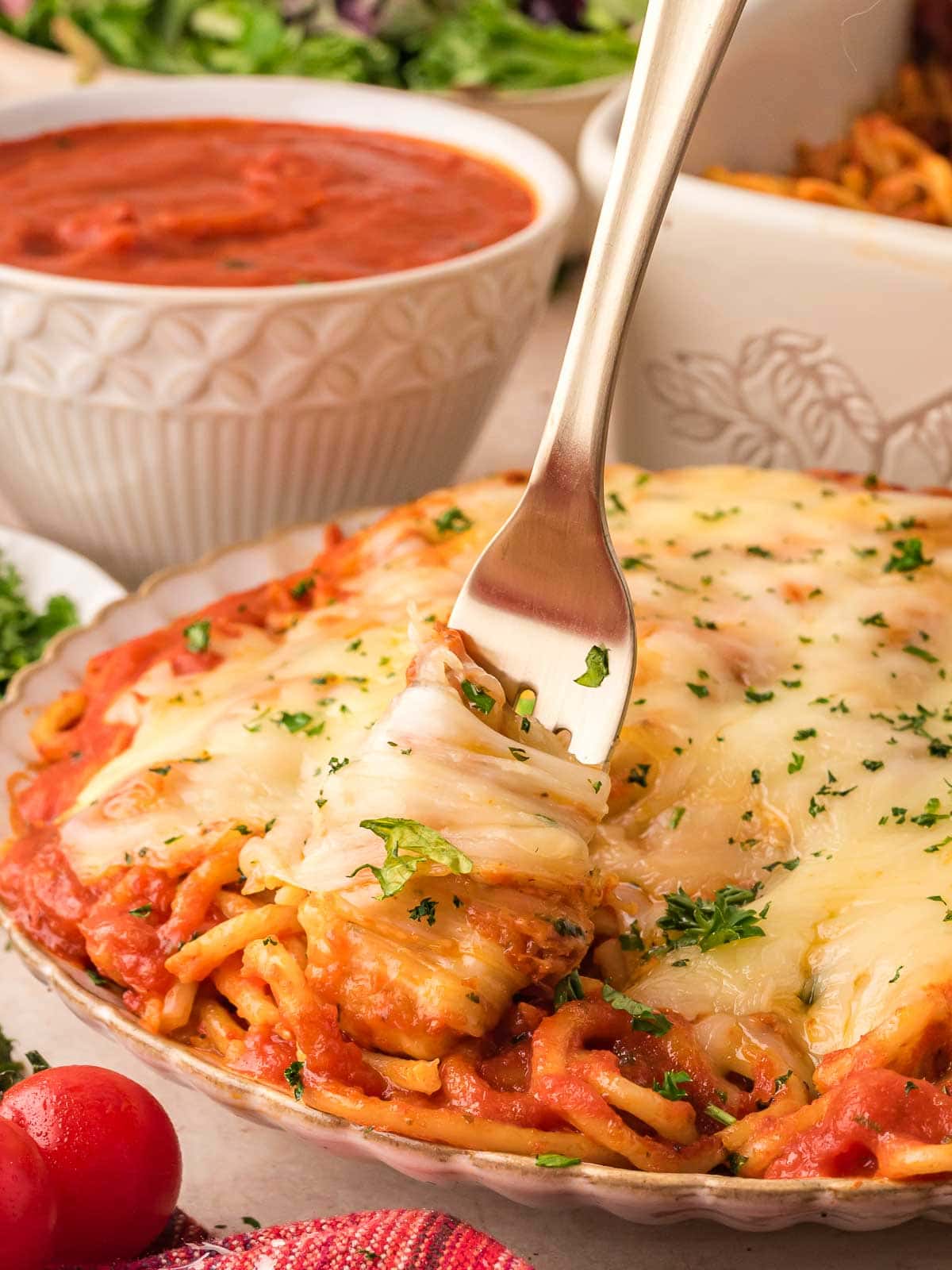 A serving of baked spaghetti on a plate with a fork, topped with melty cheese and fresh parsley, ready to eat.