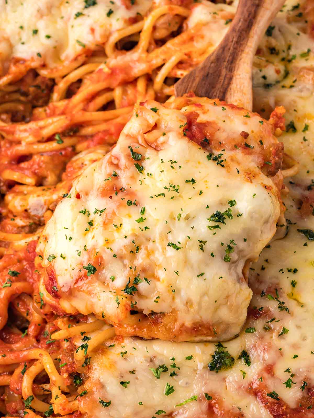 A close-up of cheesy baked spaghetti being lifted from the dish, showing gooey melted mozzarella and ground beef.