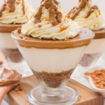 One serving of biscoff cheesecake cups in a triangle shaped bowl with whipped cream and melted biscoff poured on top.