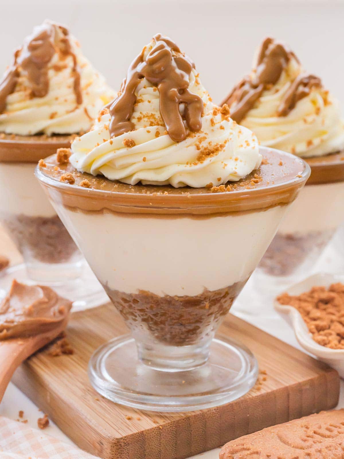 One serving of biscoff cheesecake cups in a triangle shaped bowl with whipped cream and melted biscoff poured on top.