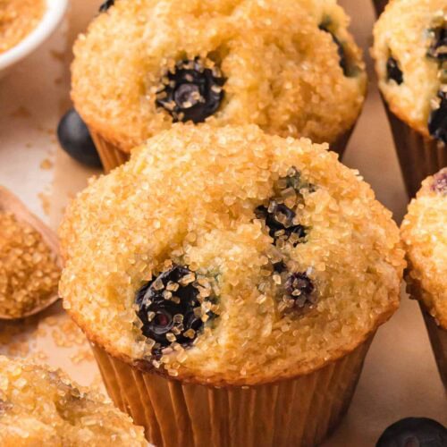Close-up of a fluffy blueberry muffin topped with coarse sugar and juicy blueberries, fresh from the oven.