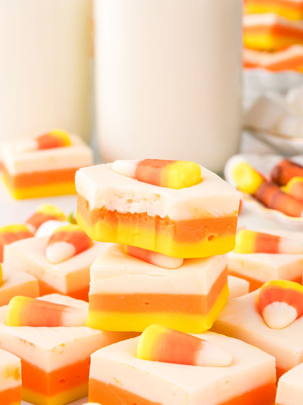 Bite taken out of a piece of Candy Corn Fudge stacked with more fudge squares around it, with milk bottles in the background.