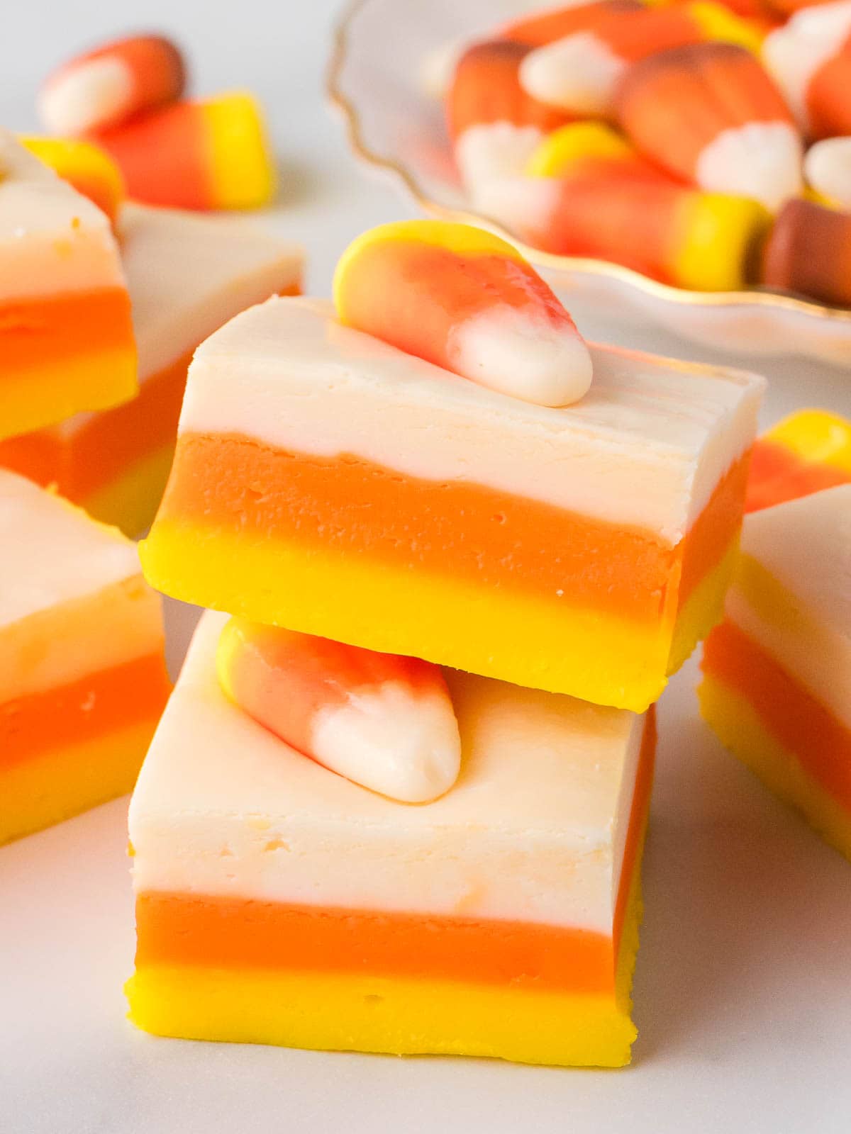 Stacked squares of Candy Corn Fudge with yellow, orange, and white layers, each topped with a single candy corn.