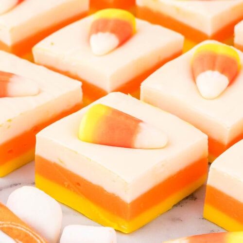 Close-up of neat fudge squares topped with candy corn, arranged in rows on a marble surface with orange napkin accents.