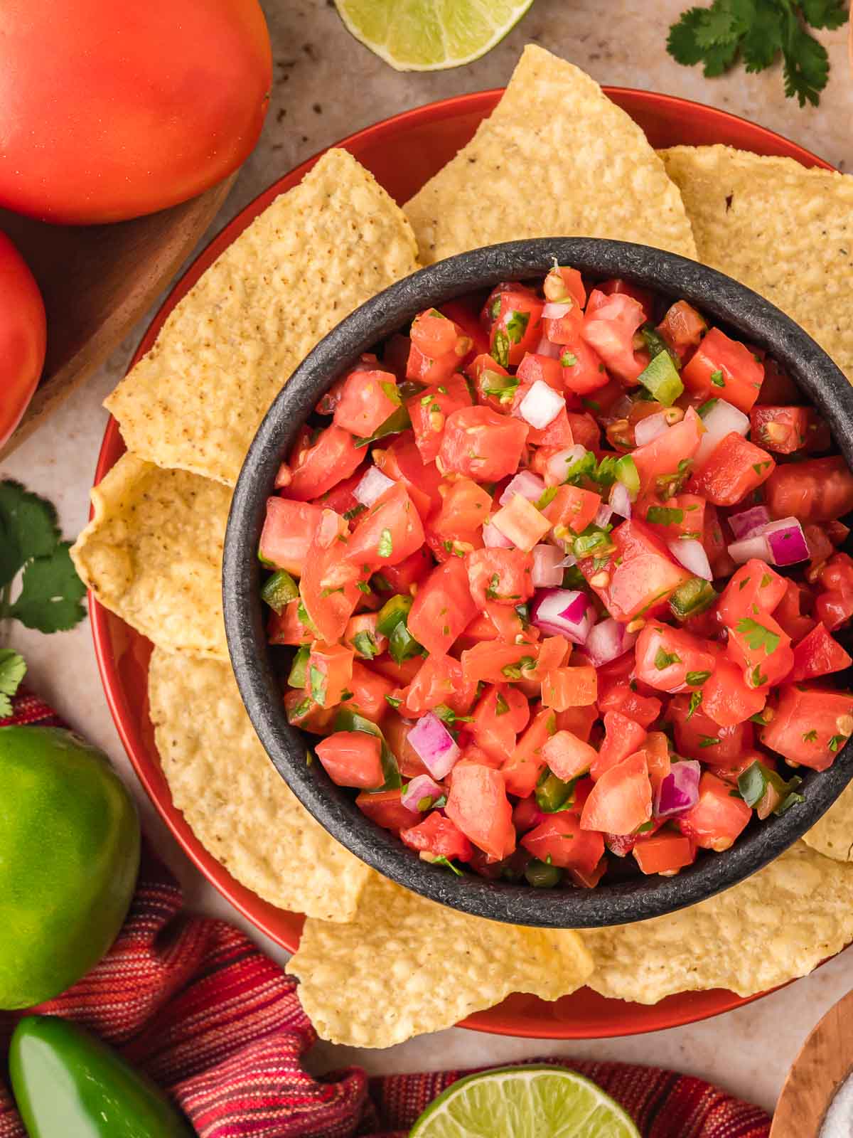 Close-up of chunky tomato salsa in a black bowl with tortilla chips arranged around the edge of the plate.