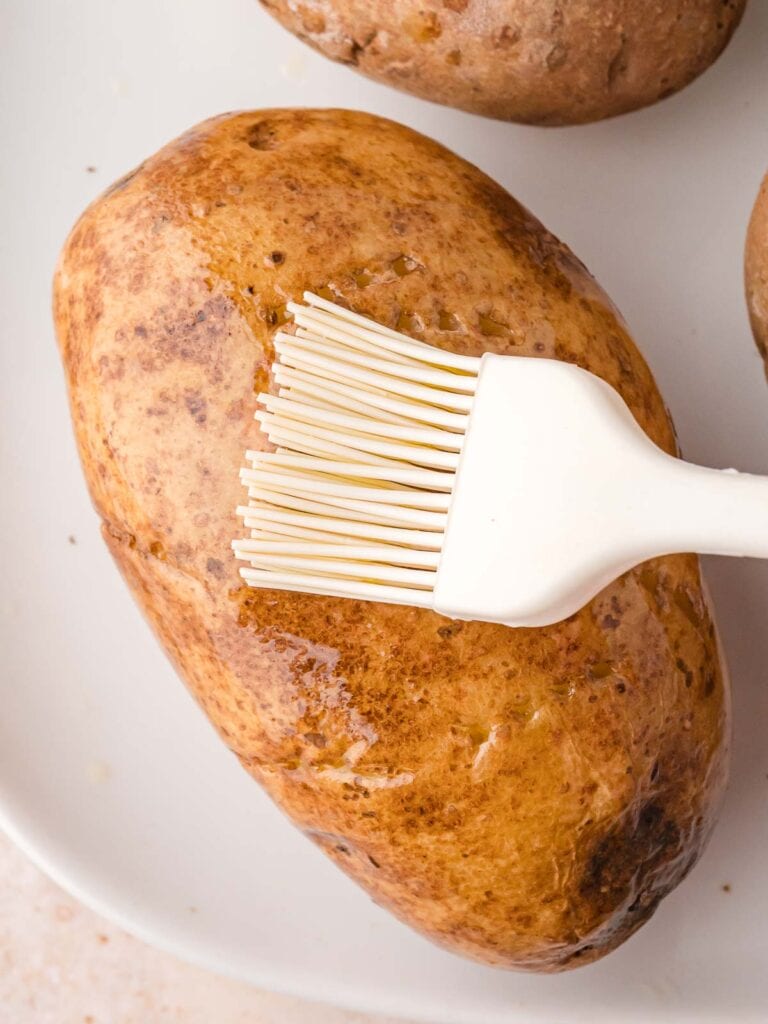 Brushing a raw russet potato with olive oil before air frying.