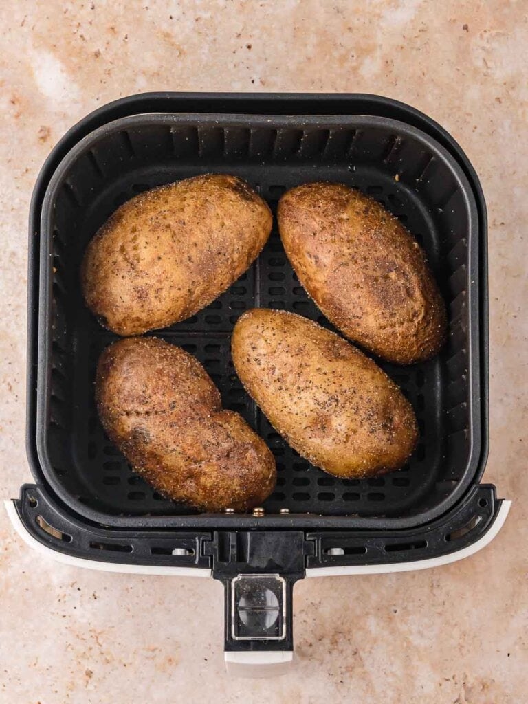 Four crispy baked potatoes resting in the air fryer basket, golden brown with seasoned skin after cooking.