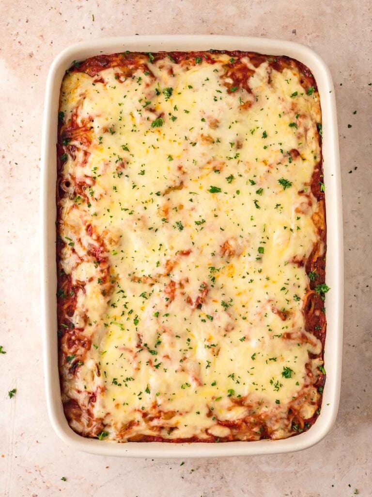 Cheesy baked spaghetti casserole just out of the oven, with melted golden cheese and parsley sprinkled on top.