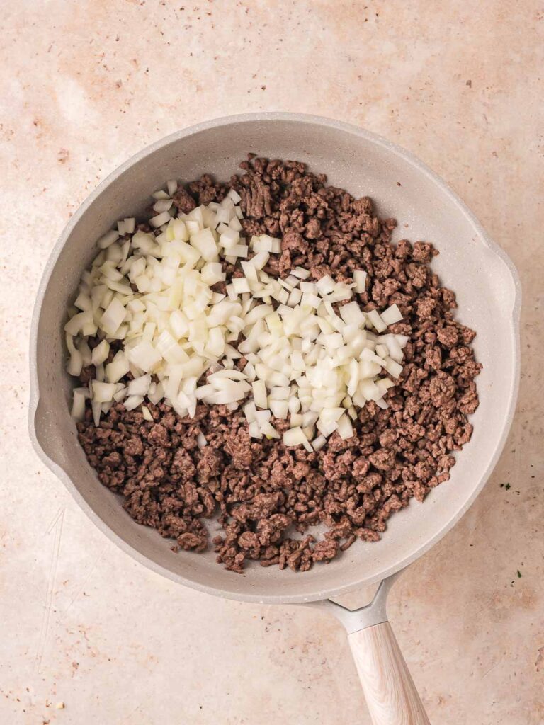 Ground beef and chopped onions sautéing together in a skillet before adding the sauce.