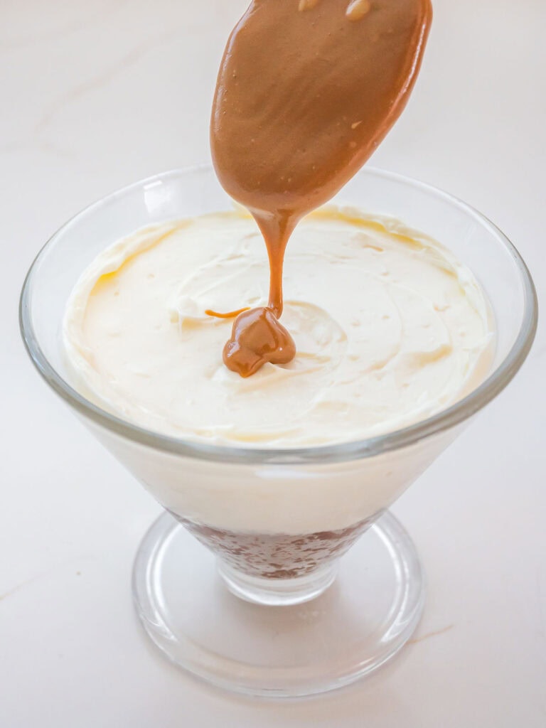 Melted biscoff cookie butter being poured onto the cheesecake filling in a serving glass.