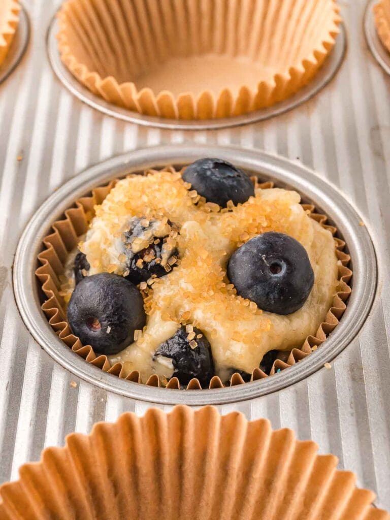 Muffin batter topped with extra blueberries and coarse sugar before baking.