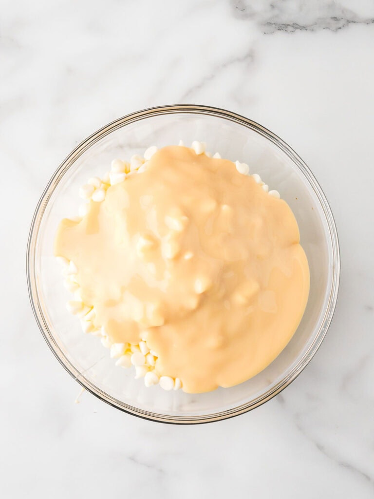 Glass bowl filled with white chocolate chips and sweetened condensed milk before microwaving, ready to make fudge.