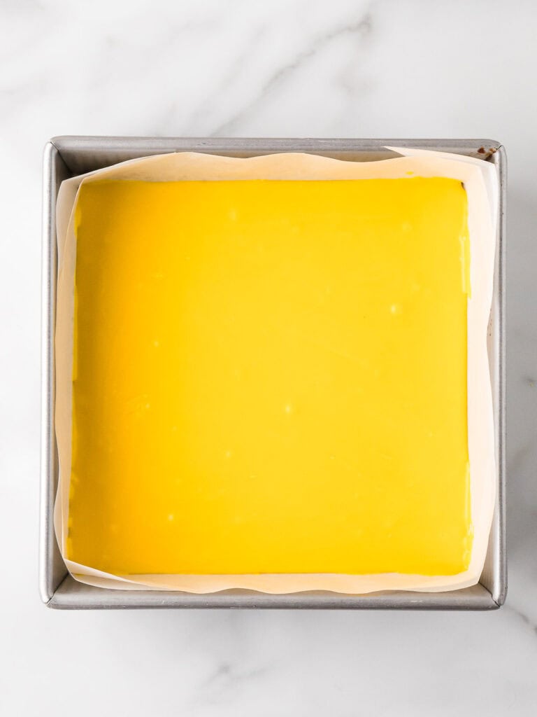 Smooth yellow fudge layer spread evenly in a parchment-lined square baking pan, setting in the fridge.