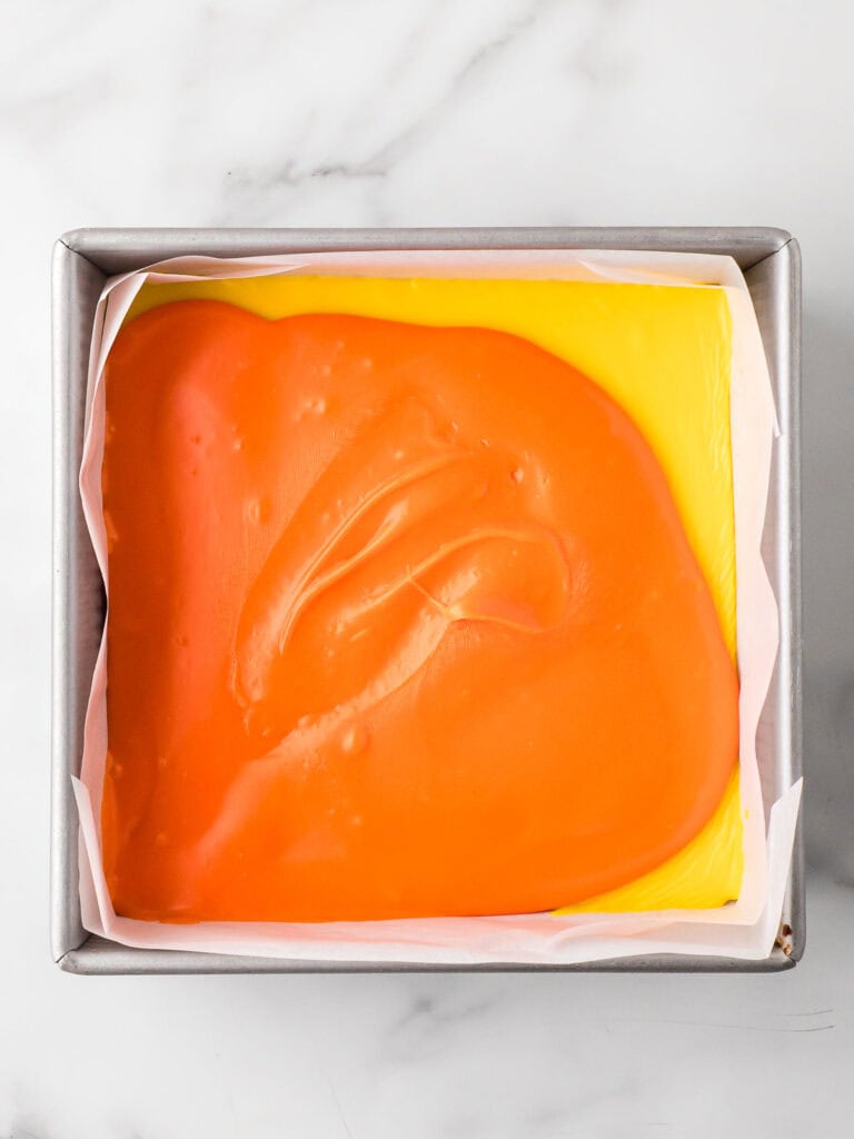 Orange fudge layer being added on top of the set yellow layer inside the baking pan.