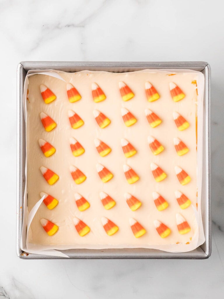 Finished layered fudge in a square pan topped with rows of candy corn, fully set and ready to slice.
