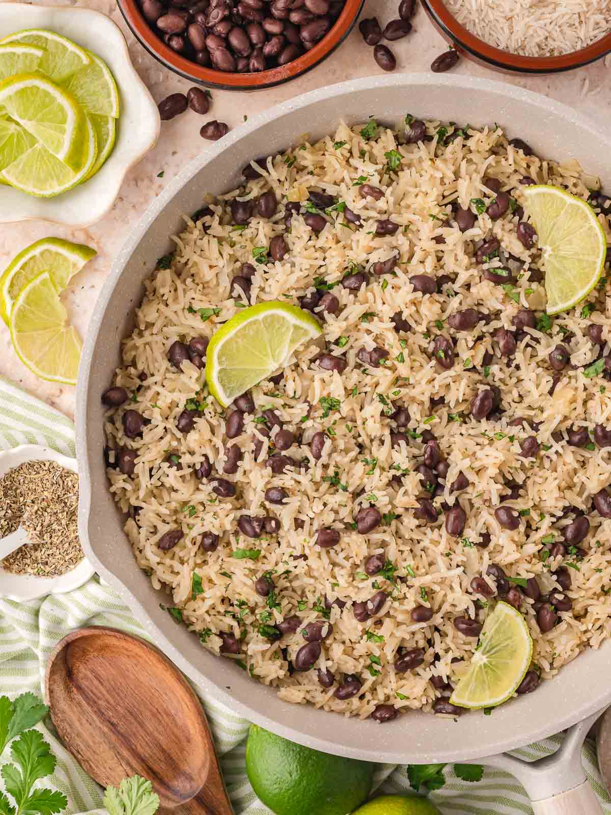 A large skillet filled with fluffy white rice and black beans, garnished with lime wedges and fresh cilantro.