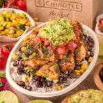 Copycat Chipotle burrito bowl in a takeout-style container filled with seasoned chicken, beans, rice, salsa, and guacamole.