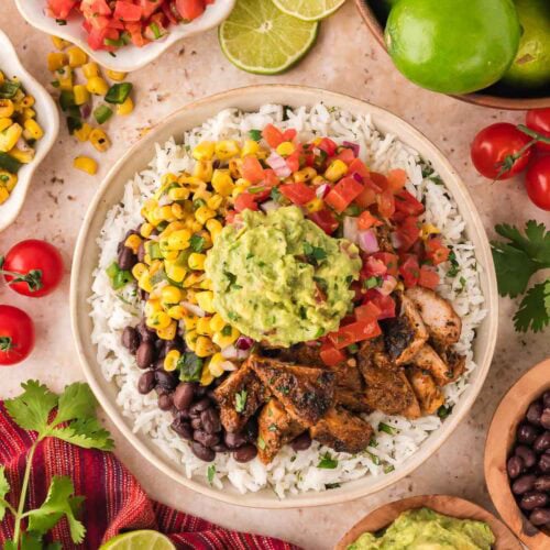 Bowl of Chipotle chicken burrito bowl topped with black beans, roasted corn salsa, fresh tomato salsa, and guacamole.