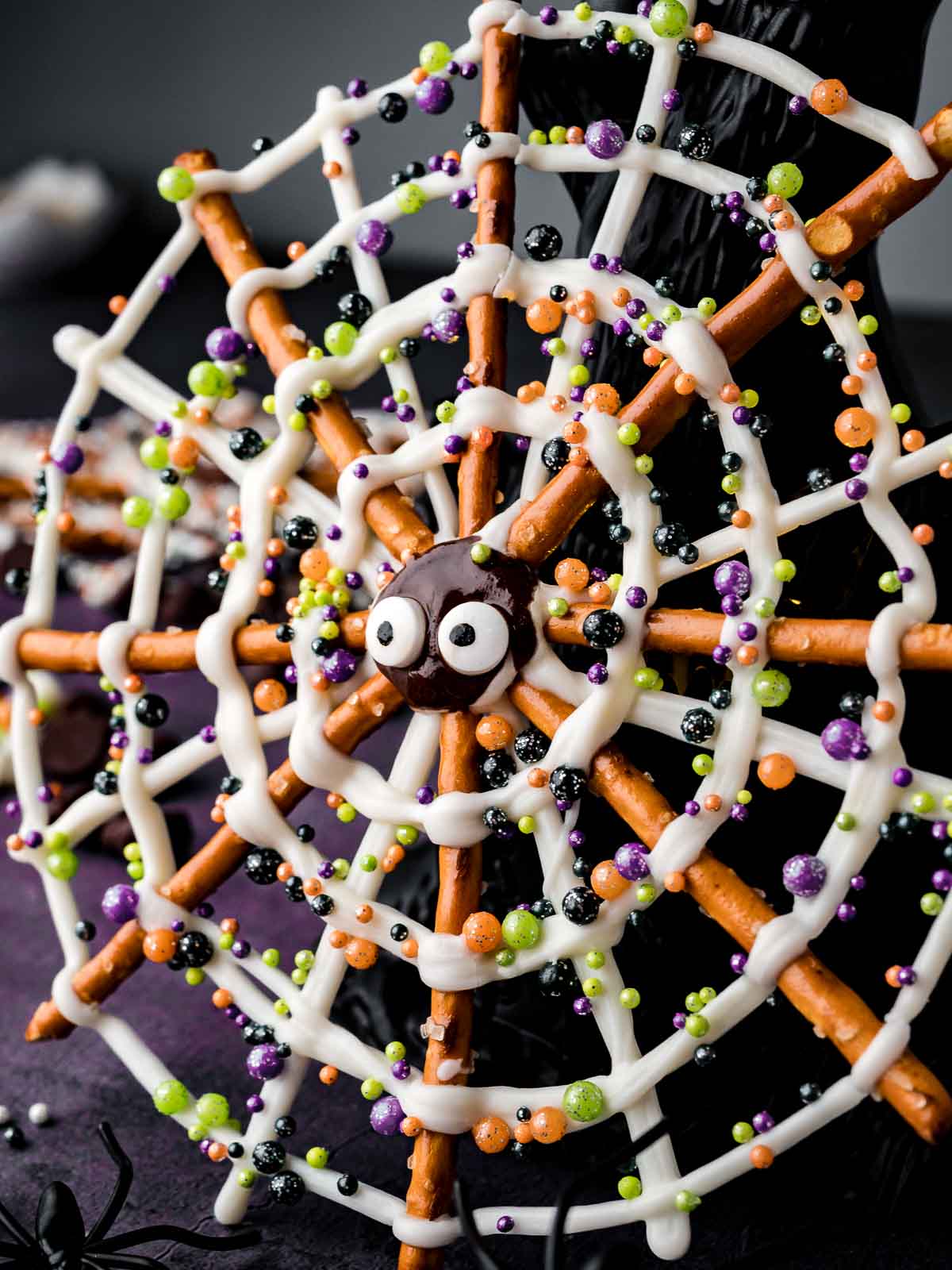 Halloween Pretzel Spider Webs on a party table with candy eyes, sprinkles, and a jack-o-lantern decoration.