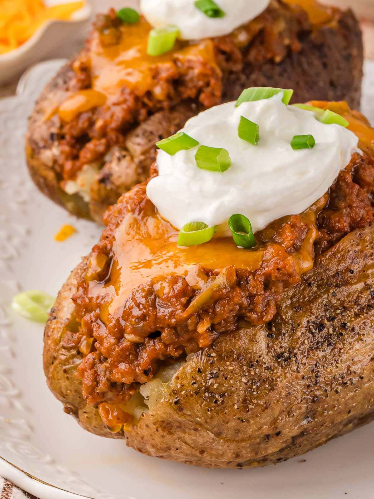 Sloppy Joe baked potato topped with melted cheddar, sour cream, and chopped green onions on a white plate.