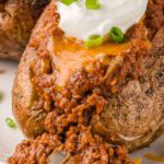 Sloppy Joe baked potato with cheddar cheese and sour cream, overflowing with saucy beef and peppers.