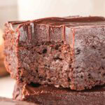 Extreme close-up of a sweet potato brownie with a bite taken out, showing the moist, fudgy chocolate center beneath the glossy ganache layer.