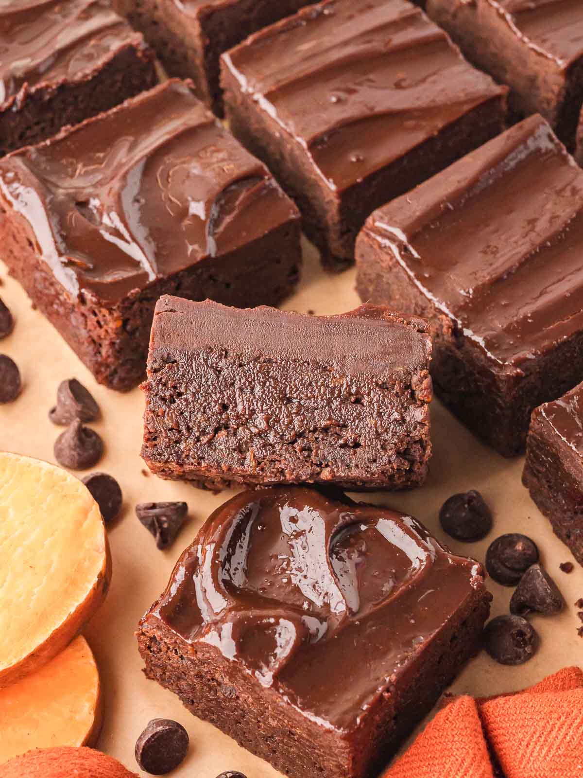 Close-up of sweet potato brownies with a shiny chocolate ganache topping, one brownie turned on its side to show the rich, fudgy texture inside.