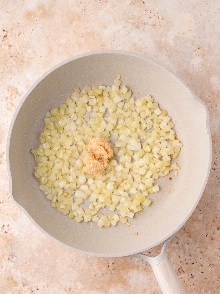 Chopped onion sautéing in a skillet with freshly minced garlic added to the center.