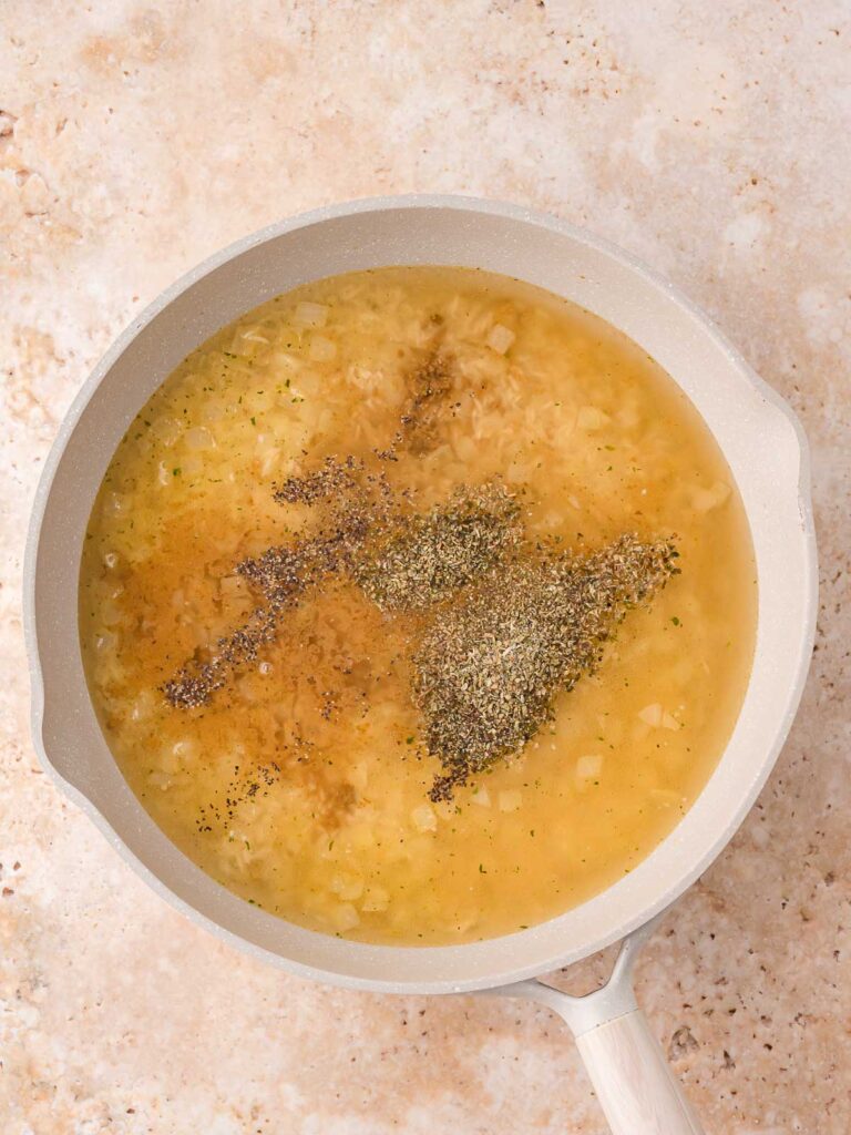 Broth poured over the rice mixture in the skillet with seasonings sprinkled on top before simmering.