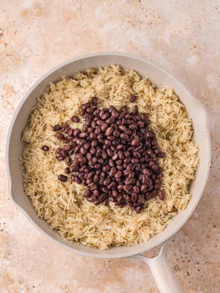 Drained black beans sitting on top of the cooked rice, just before being stirred together.