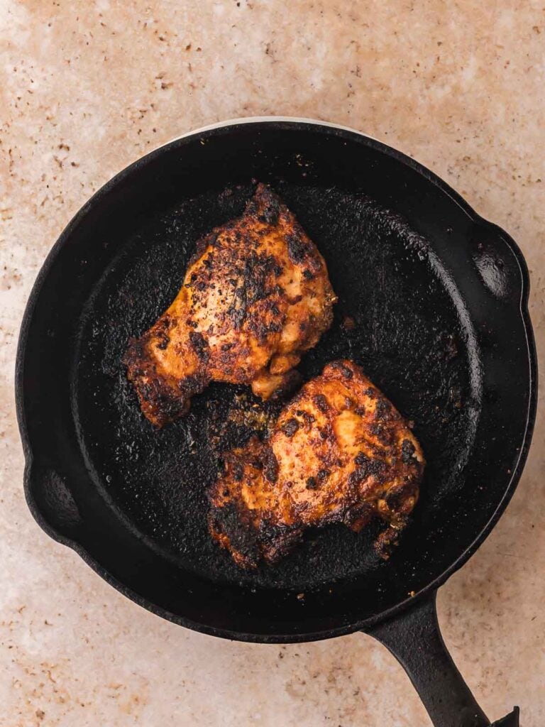 Seasoned chicken thighs cooking in a hot cast iron skillet.