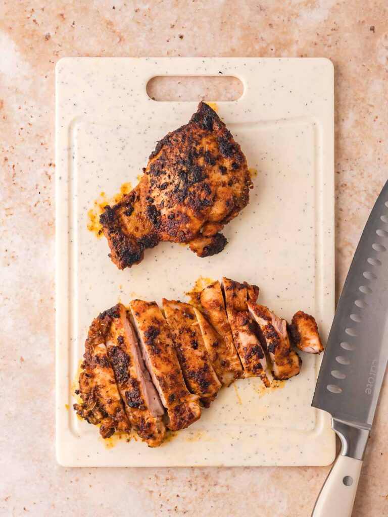 Cooked chicken thigh sliced on a cutting board, ready for burrito bowls.