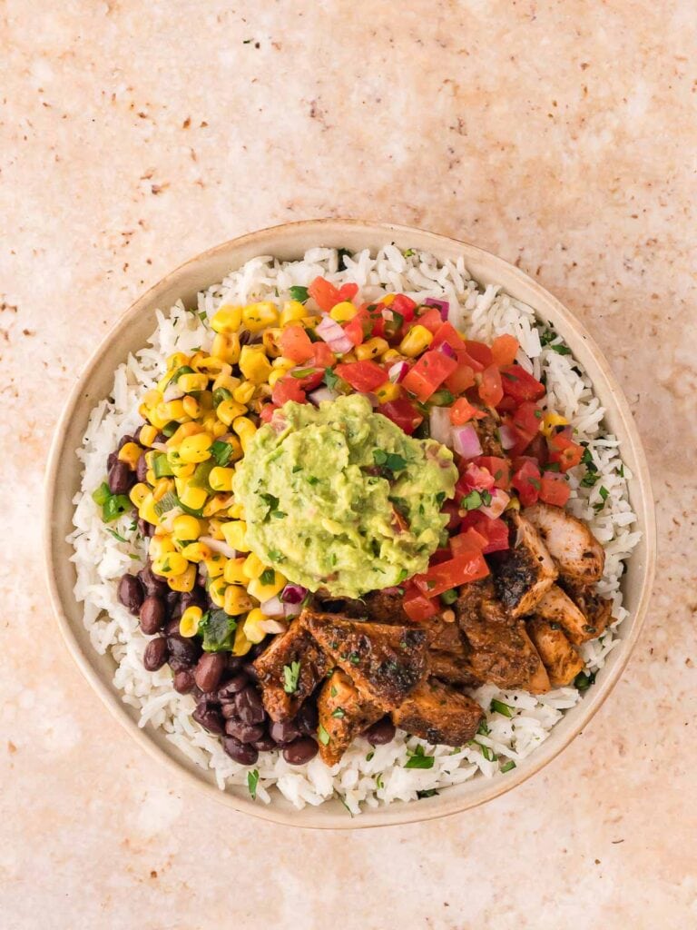 Finished Chipotle chicken burrito bowl with rice, beans, chicken, roasted corn salsa, tomato salsa, and guacamole.