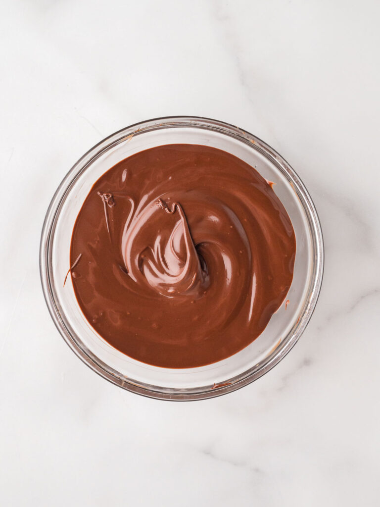 Glass bowl filled with smooth, freshly melted chocolate for dipping marshmallow pops.