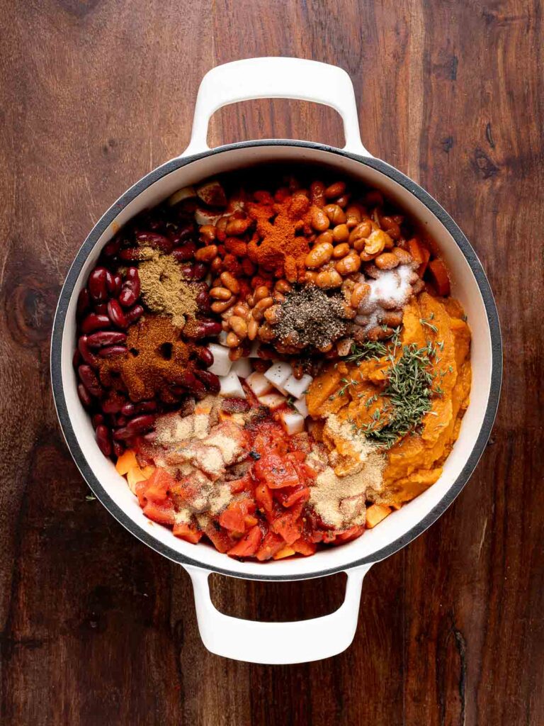 ngredients for pumpkin chili added to the pot, including beans, tomatoes, pumpkin purée, spices, and fresh thyme.