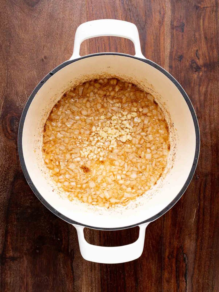 Diced onions and minced garlic sizzling in bacon fat at the bottom of a Dutch oven.