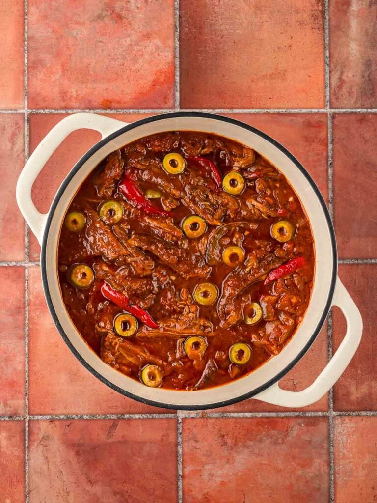 Final dish of shredded flank steak stewed in tomato sauce with red peppers and sliced green olives, ready to serve.