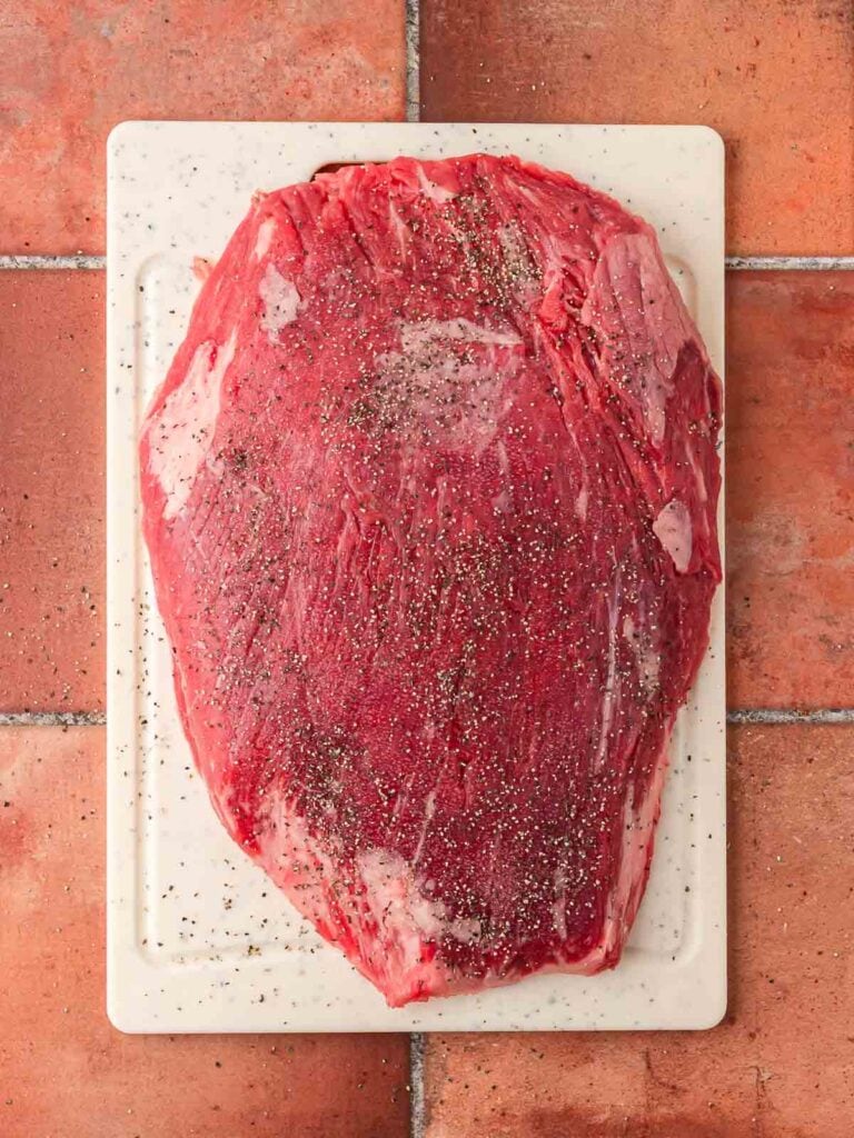 Raw flank steak seasoned with salt and pepper on a white cutting board, ready for searing.