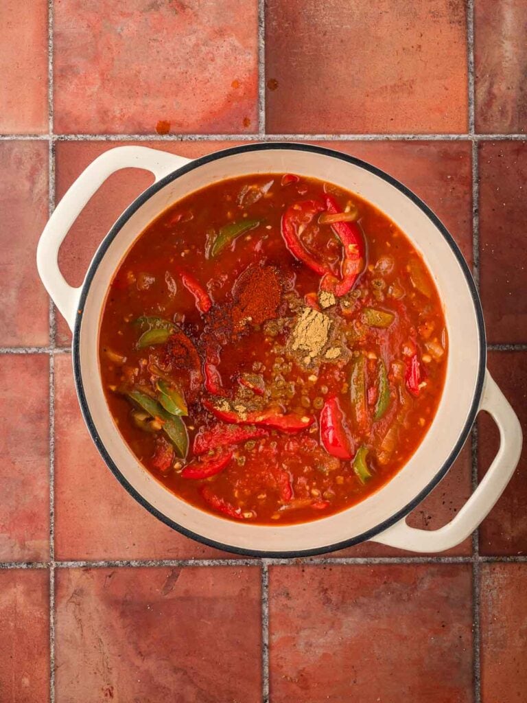 Crushed tomatoes, spices, and bay leaves added to the pot, forming the base of the rich tomato sauce.