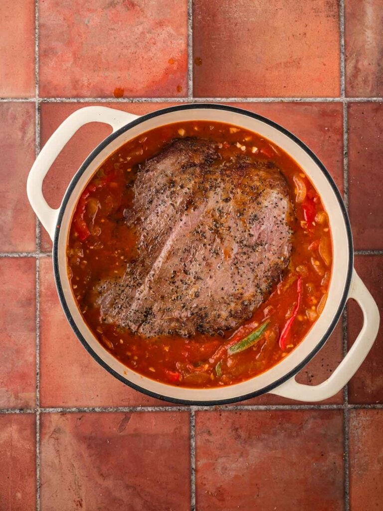 Searing flank steak returned to the Dutch oven and nestled into the tomato sauce mixture.