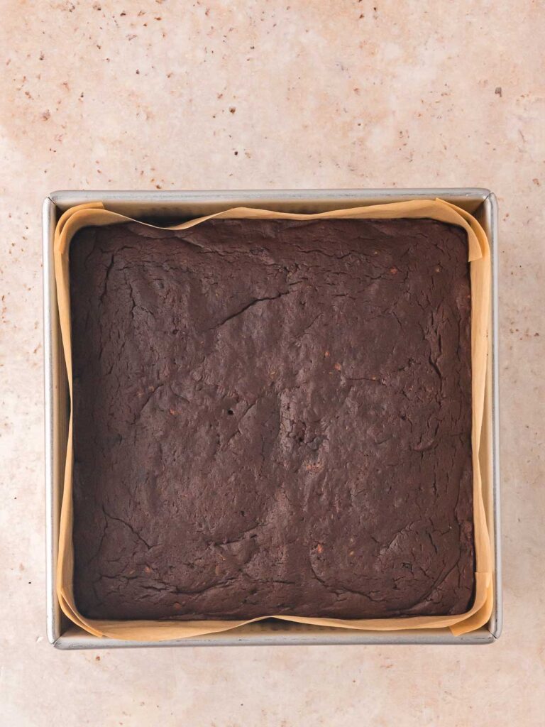 Baked sweet potato brownie base cooling in a parchment-lined square baking pan before adding ganache.