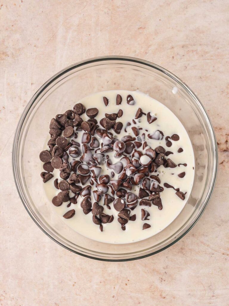 Chocolate chips and heavy cream in a glass bowl, ready to be mixed into a smooth ganache for brownies.