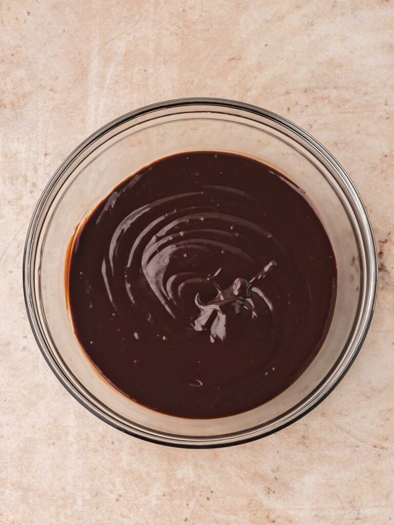 Glossy chocolate ganache in a glass bowl after being whisked until smooth and creamy.