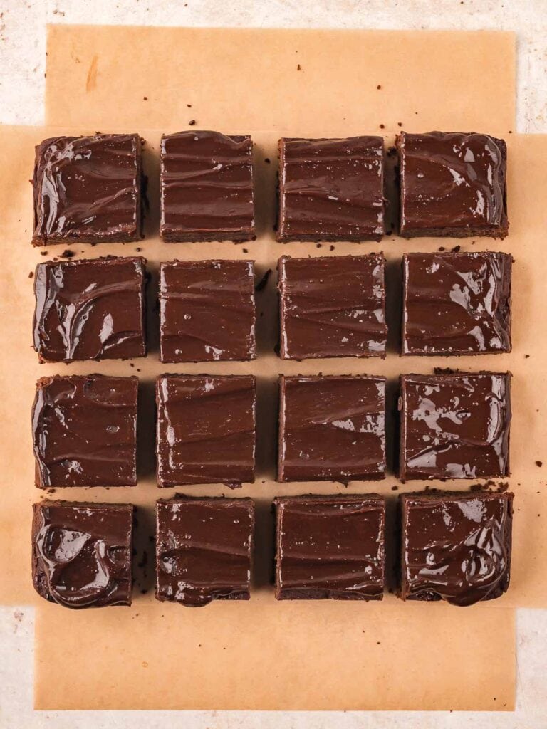 Sixteen squares of sweet potato brownies topped with shiny ganache, arranged neatly on parchment paper.