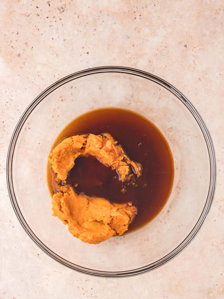 Mashed sweet potato and maple syrup in a glass mixing bowl, ready to be combined for sweet potato brownies.