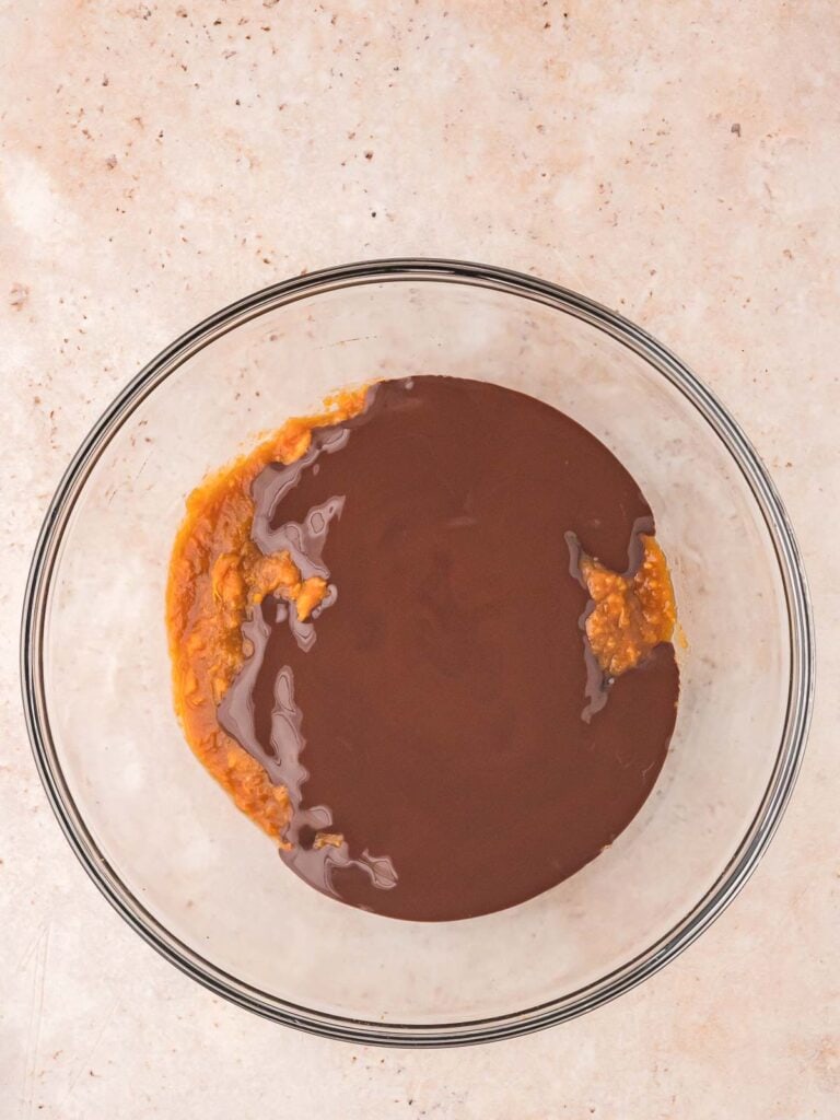 Melted chocolate poured over mashed sweet potato mixture in a glass bowl for sweet potato brownies.