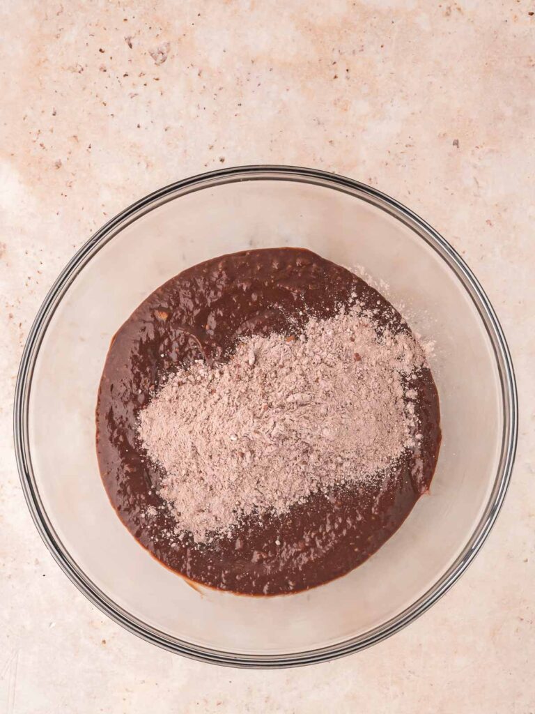 Dry ingredients sitting on top of the wet chocolate mixture, ready to be folded together for sweet potato brownies.