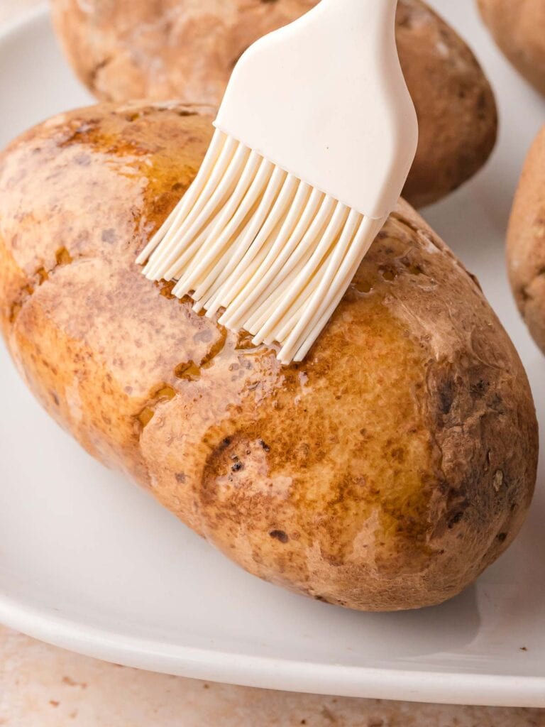 Potato being brushed with olive oil before cooking.